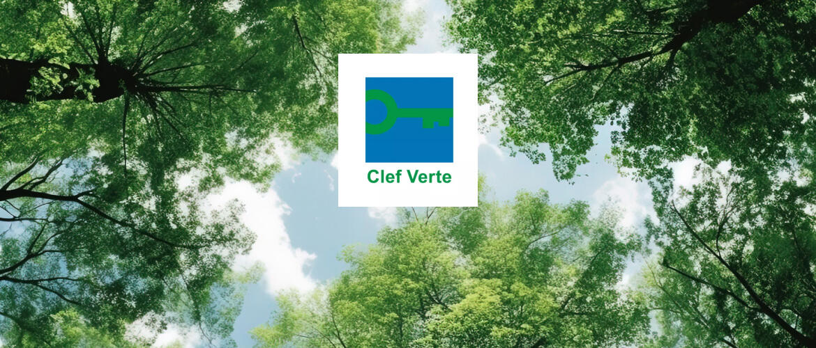 Vue en contre-plongée des cimes des arbres avec un ciel bleu en arrière-plan, mettant en valeur le logo du label environnemental 'Clef Verte' au centre, symbolisant l'engagement d'Appart'City pour le tourisme durable et respectueux de l'environnement.