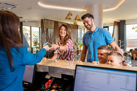 Smiling family at the reception of an Appart’City aparthotel, receiving the keys to their room, representing a CSE offer for a family stay