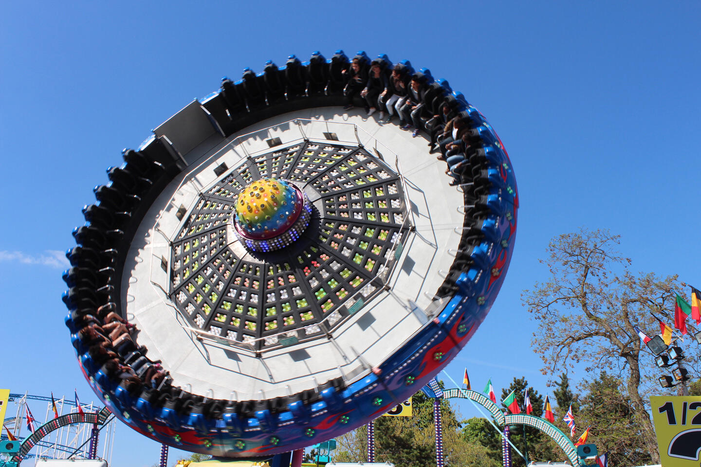 Spinning ride at the Foire du Trône with people seated around, blue sky in the background