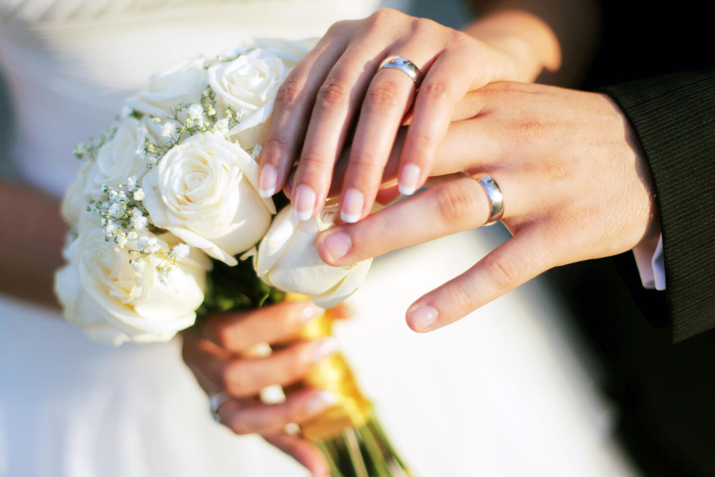 Mains d'un couple marié avec leurs alliances, la mariée tenant un bouquet de roses blanches, au Salon du Mariage de Paris