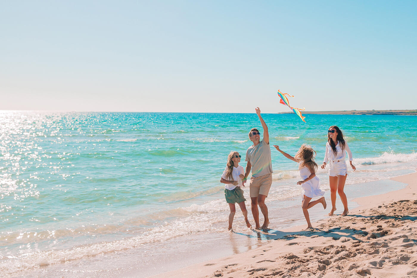 Familie, die mit einem Drachen an einem sonnigen Strand spielt, mit dem türkisfarbenen Meer im Hintergrund während ihres Urlaubs.