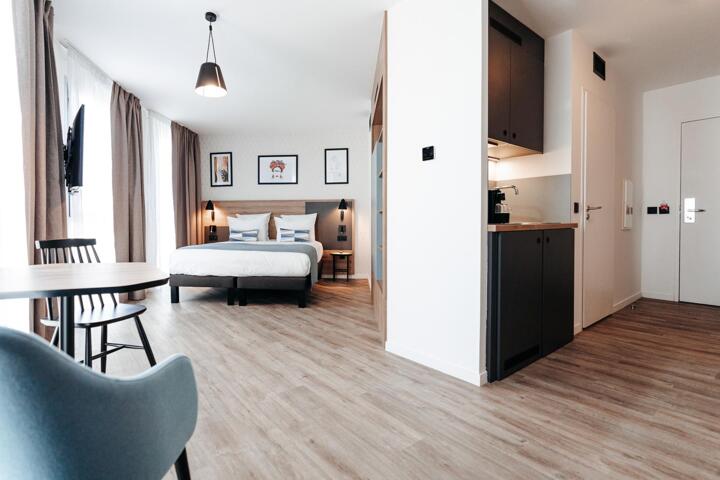 Modern and spacious studio-type room at Appart'City, featuring a large double bed, a fully equipped kitchenette, a sitting area, and elegant decor.