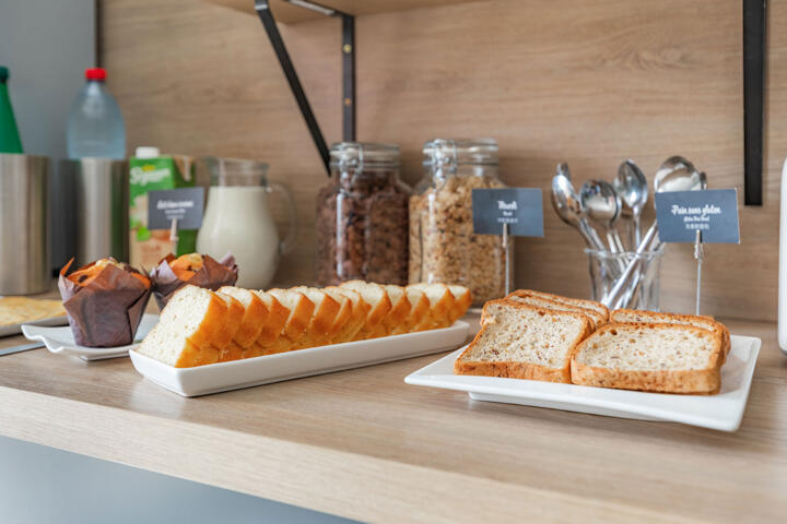 Frühstücksauswahl in einem Aparthotel der Classic-Kollektion mit geschnittenem Brot, Muffins, Müsli und Milch.