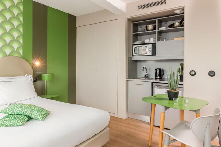 Studio moderne et coloré dans l'appart'hôtel Appart'City Vélizy, avec kitchenette équipée, décoration verte et lit confortable.