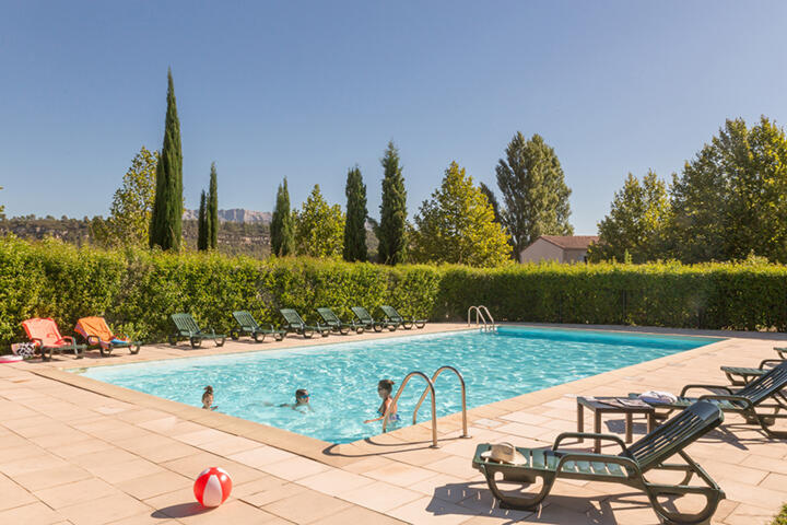 Piscine extérieure entourée de transats et de verdure à l'appart'hôtel Appart'City, idéale pour se détendre sous le soleil.